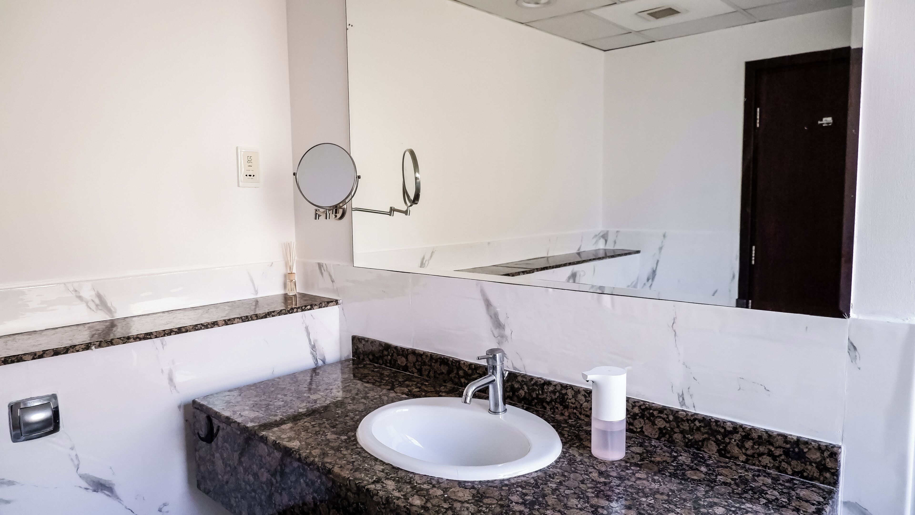Un baño con lavamanos blanco, encimera de granito y un espejo grande.