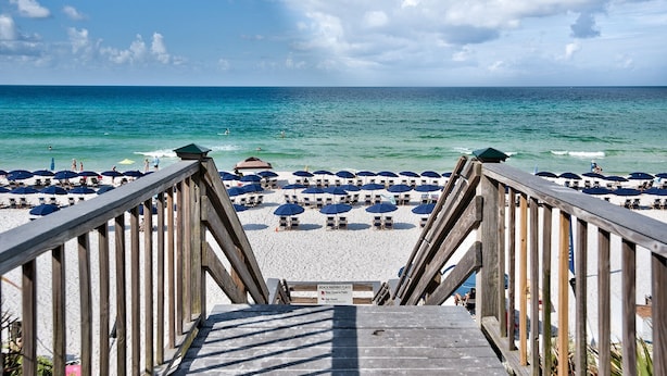 A wooden boardwalk leading to a beach with rows of umbrellas and beach chairs.