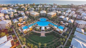 A resort with a central pool, multiple buildings, and a view of the ocean.