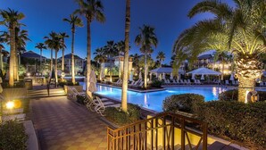 A pool area with lounge chairs, palm trees, and a well-lit pathway leading to the pool.