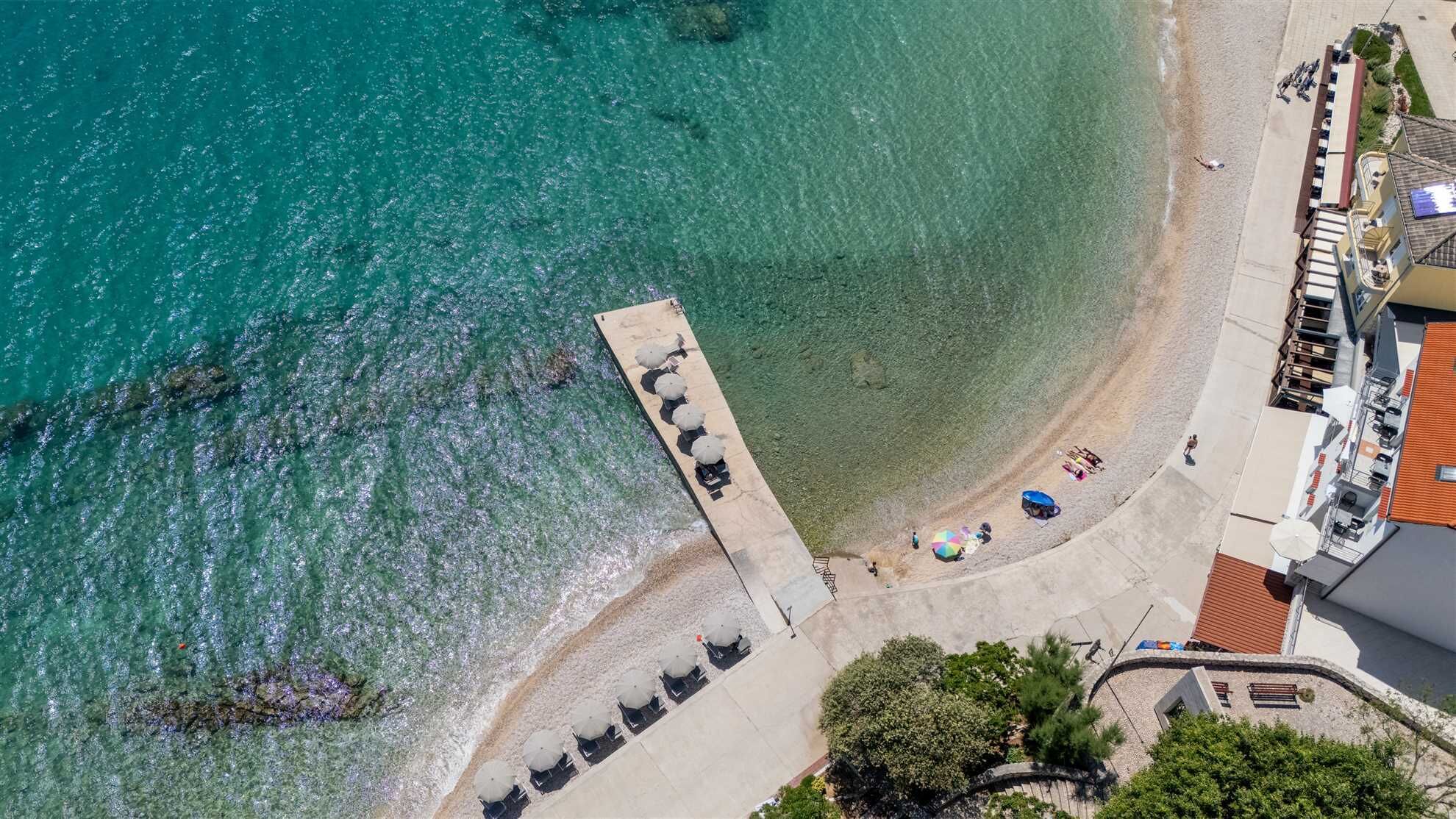 An aerial view of a coastal area with a pier, beach, and adjacent buildings.