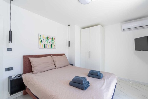 A modern bedroom with a bed, a wardrobe, a TV, and a wall-mounted air conditioner.