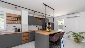A modern kitchen with marble countertops, wooden shelves, and a bar area with bar stools.