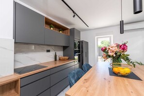 A modern kitchen with a wooden countertop, grey cabinets, a built-in oven, and a dining area with a table and chairs. - Villa Marevia by Aneo Travel (Baska)
