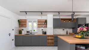 A modern kitchen with marble flooring, grey cabinets, wooden shelves, and a central island with a sink.