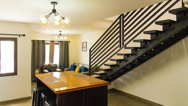 A modern kitchen with a central island, a dining area with a sofa, and a staircase with a black railing. - Casa SOFIA, spacious, safe, easy access, pets welcome  (Santa Rosa de Copán)