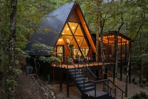 A cabin with a triangular roof, a wooden deck, and a staircase leading to a second level. - Evergreen Dreams | A-Frame Retreat + Hot Tub/Sauna (Polk County)