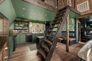 A loft-style kitchen with a wooden staircase, green cabinets, and a view of the outdoors. - Evergreen Dreams | A-Frame Retreat + Hot Tub/Sauna (Polk County)