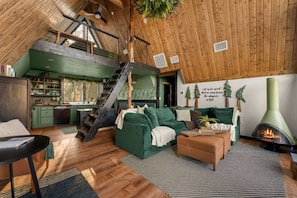 A loft-style living space with a staircase, green sofa, and a fireplace. - Evergreen Dreams | A-Frame Retreat + Hot Tub/Sauna (Polk County)