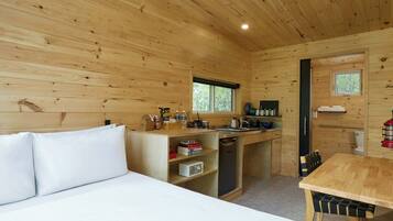 A compact wooden cabin with a bed, a kitchenette, and a dining area.