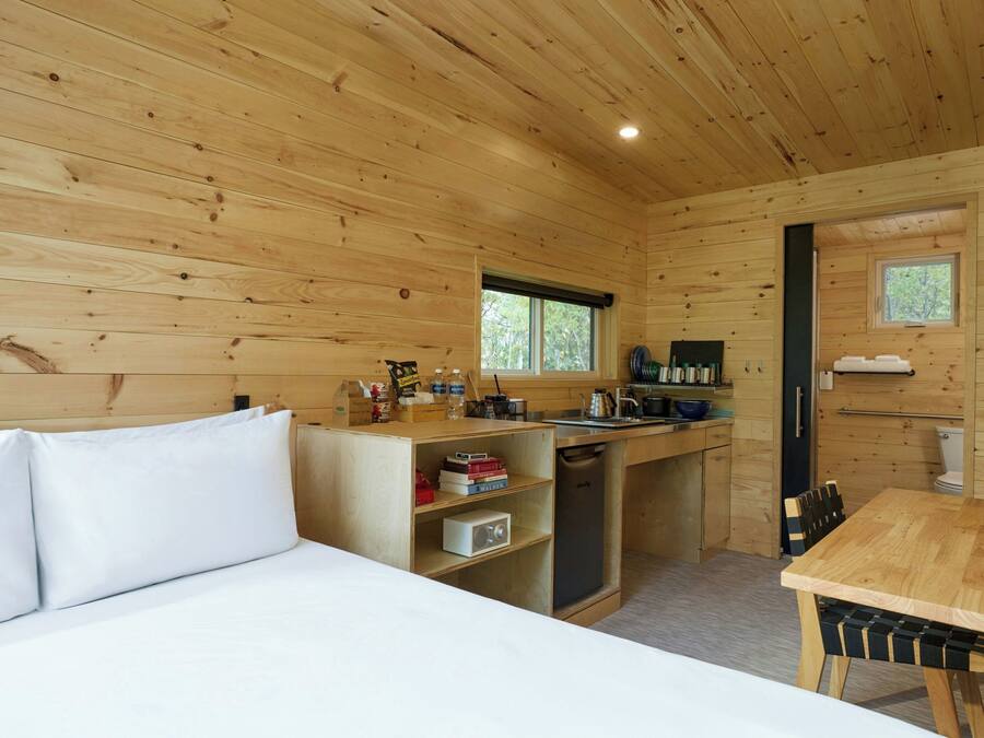 A compact wooden cabin with a bed, a kitchenette, and a dining area.