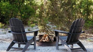 To Adirondack-stole placeret over foran et bålsted i et skovområde.
