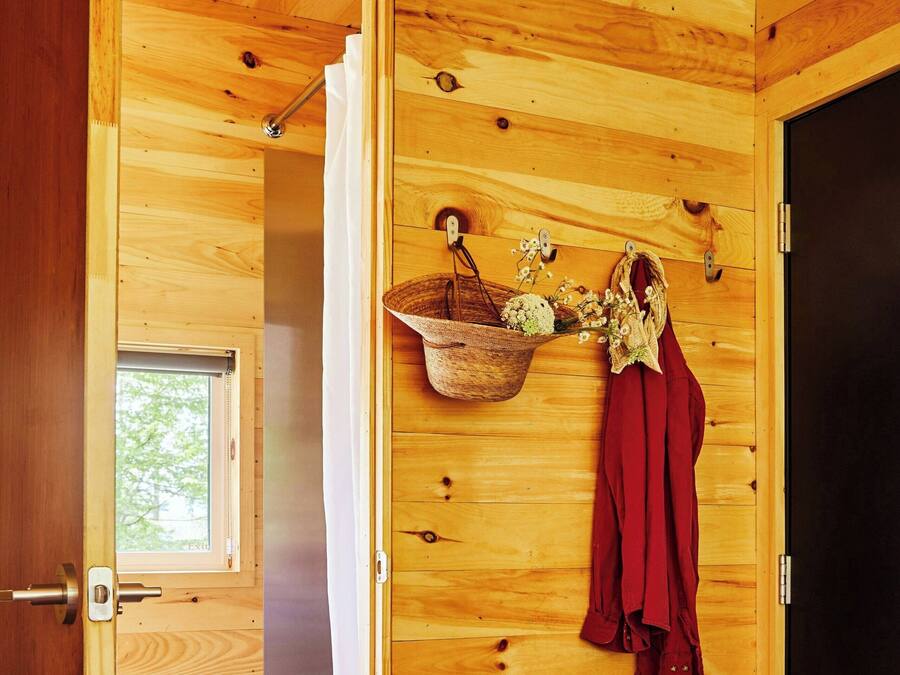 Una habitación de madera con ducha, un ventanal pequeño, una cesta de flores y un par de zapatos en el suelo.