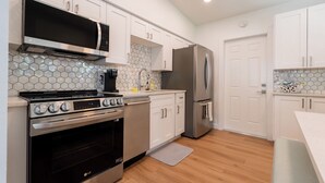 Una cocina moderna con armarios blancos, una estufa de acero inoxidable, un microondas y un refrigerador.