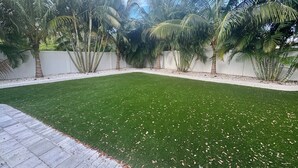 Un césped cuidado con palmeras y una valla blanca.