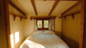 Une chambre à coucher avec un lit, des poutres en bois, une fenêtre avec des rideaux et une vue sur la verdure à l’extérieur.