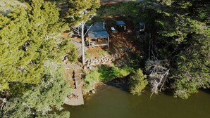Un chalet isolé, doté d’une terrasse et d’un petit quai, entouré d’une forêt dense et bordé par un plan d’eau.