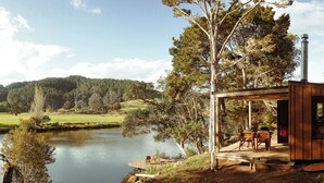 Un chalet rustique doté d’une terrasse donnant sur un lac, entouré d’arbres et d’un paysage vallonné.