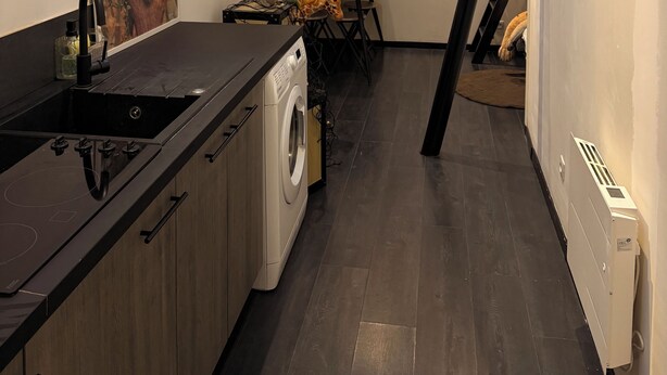 Una cocina moderna con encimera negra, lavadora y comedor con mesa y sillas.