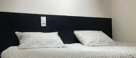 A bedroom with a bed, a black headboard, a skylight, and a white wall.