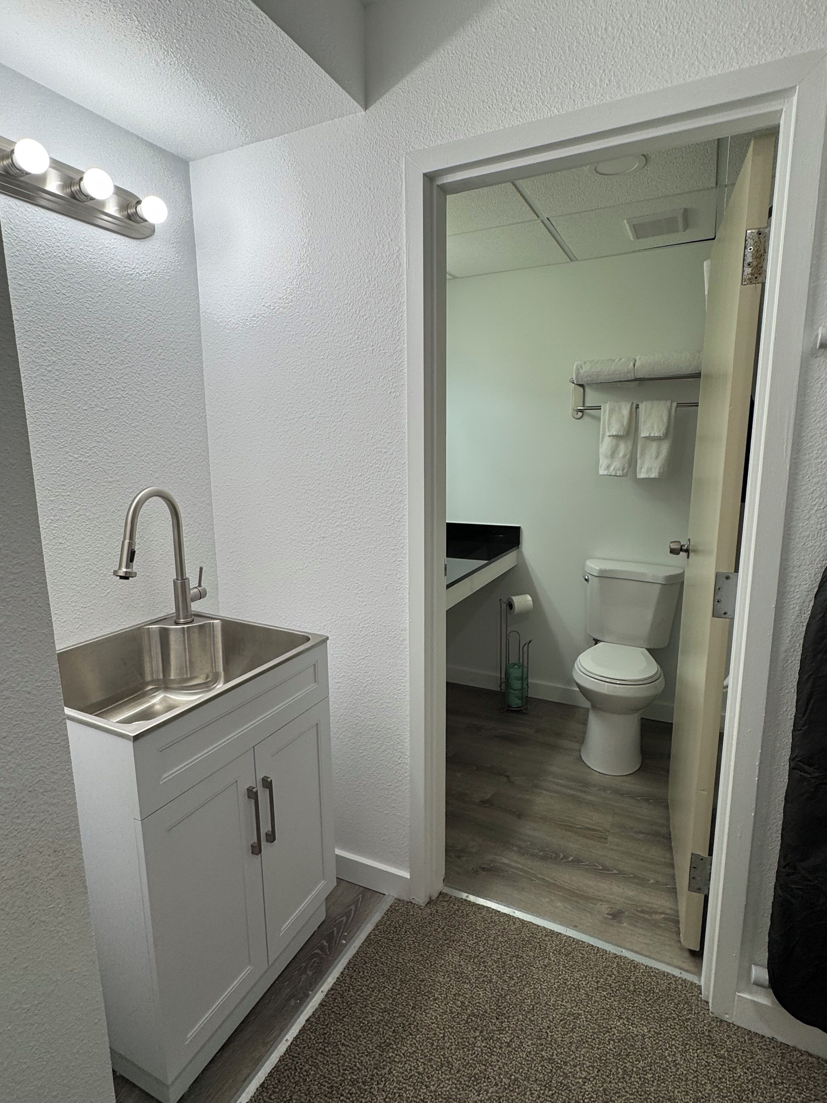 A modern bathroom with a white sink, vanity, and a toilet visible through an open door.