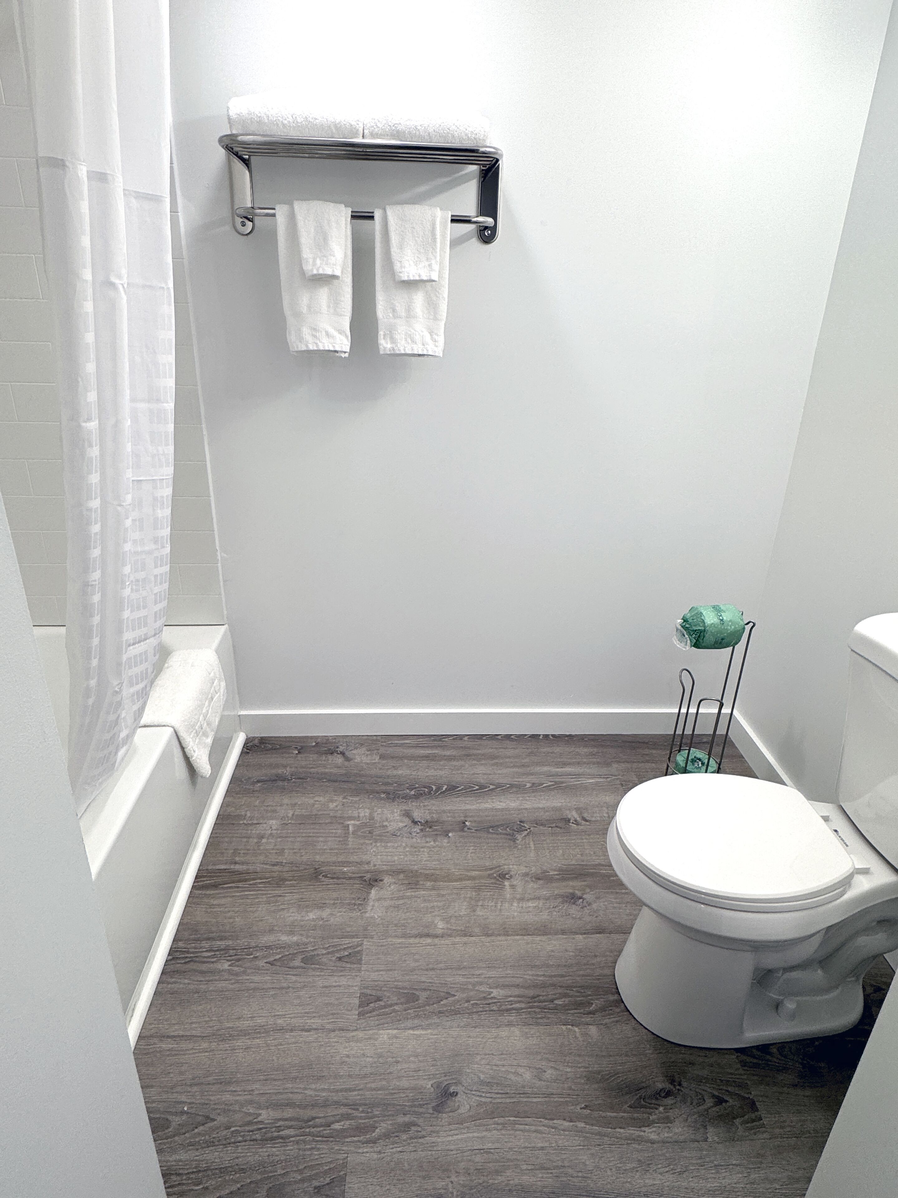 A bathroom with a white toilet, a wooden floor, a shower curtain, and a towel rack with two towels.