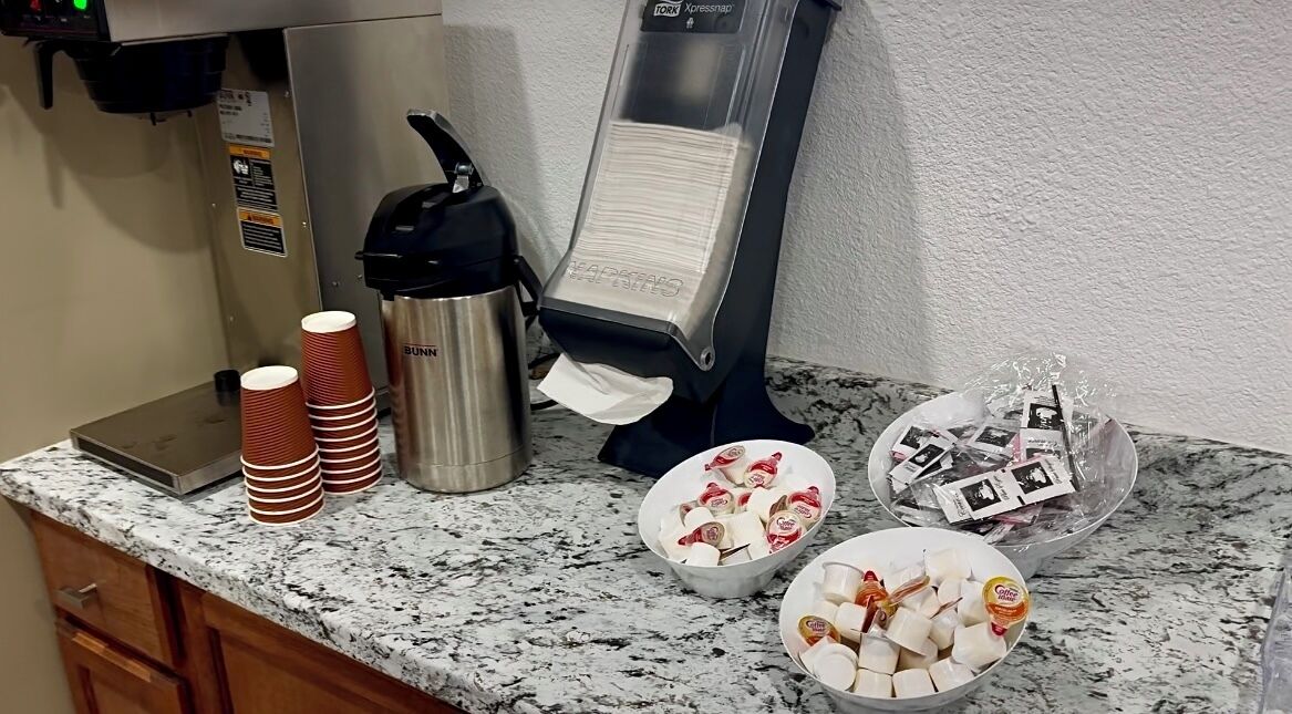 A kitchen counter with a coffee machine, disposable cups, and bowls of food items.
