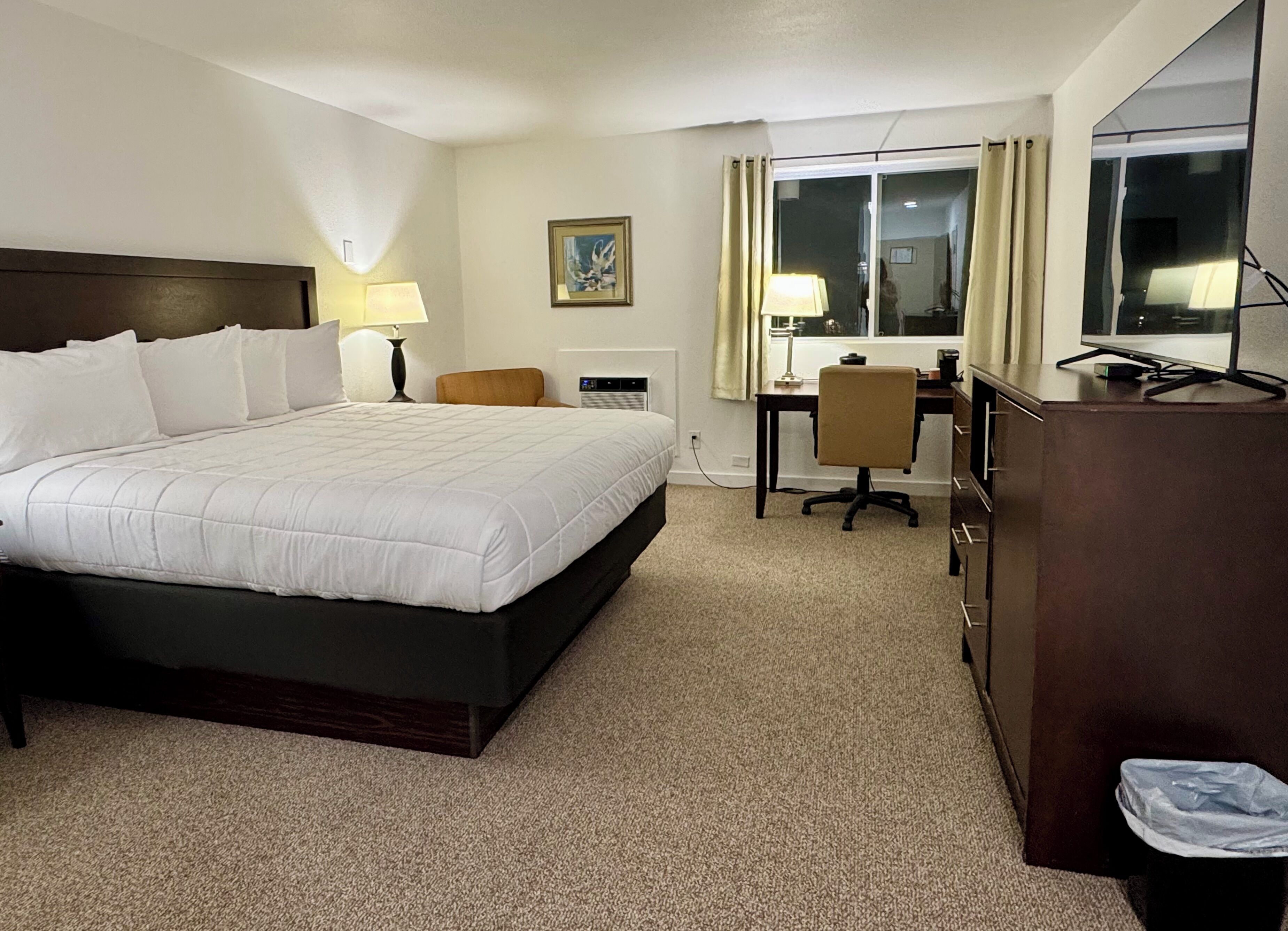 A hotel room with a large bed, a desk, a chair, a TV, and a window with curtains.