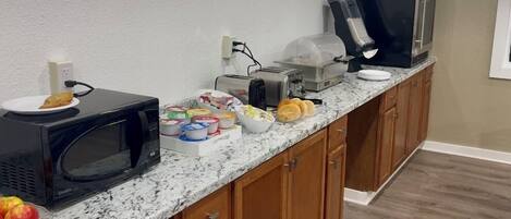 Una cocina con microondas, tostadora, cafetera y televisor sobre la encimera.