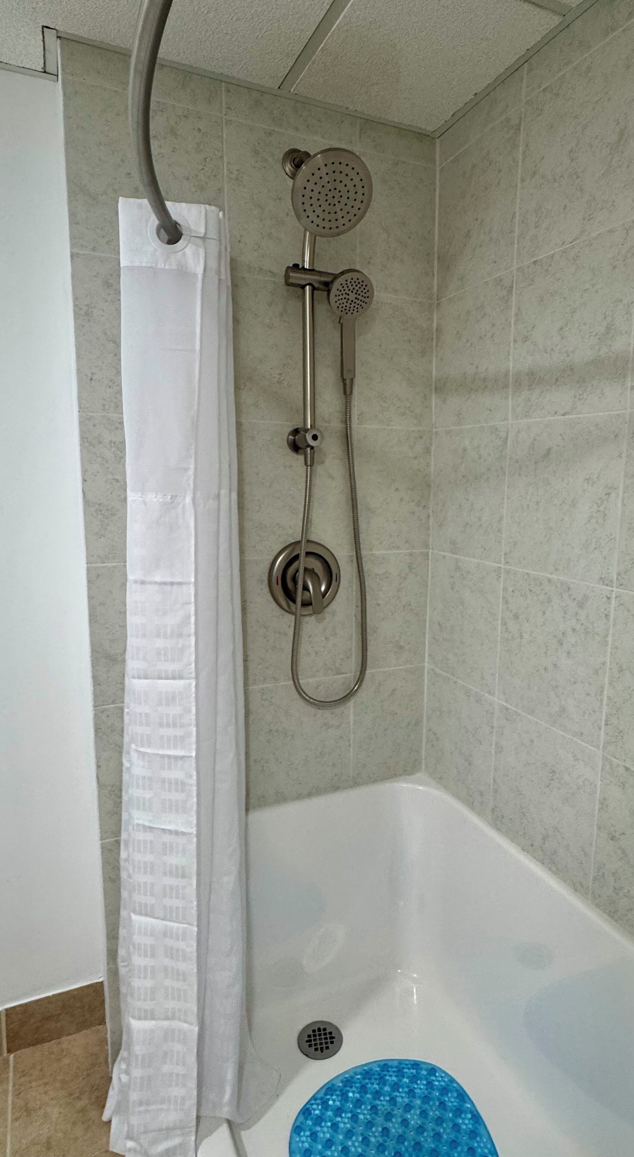 Un baño con ducha, bañera y cortina blanca.