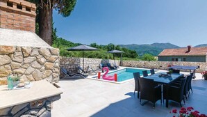 Un espace aménagé au bord de la piscine, avec des murs en pierre, une table, des chaises et des parasols.