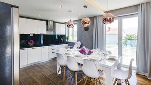 Une cuisine moderne avec des meubles blancs, un plan de travail noir et un coin repas aménagé pour six personnes, avec des chaises blanches.