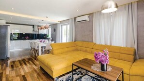 Un salon moderne avec un canapé jaune, une table basse en bois et un coin repas comprenant une table et des chaises blanches.
