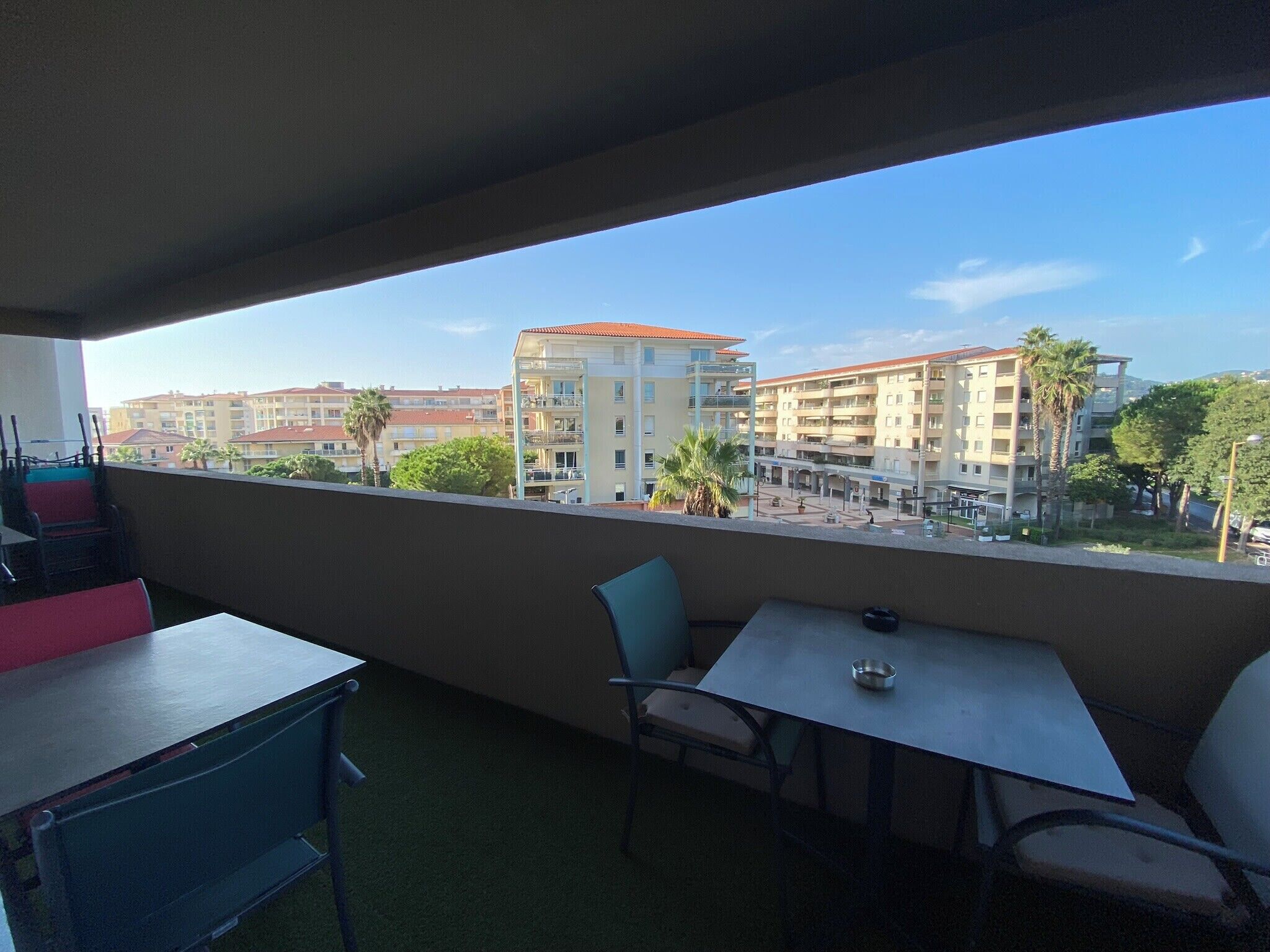 Un balcón con mesa y sillas, con vistas a una zona residencial con edificios y palmeras.
