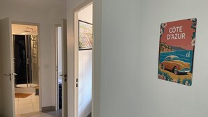 Un couloir avec une douche, une porte donnant sur une pièce et un mur orné d’une enseigne « Côte d’Azur ».