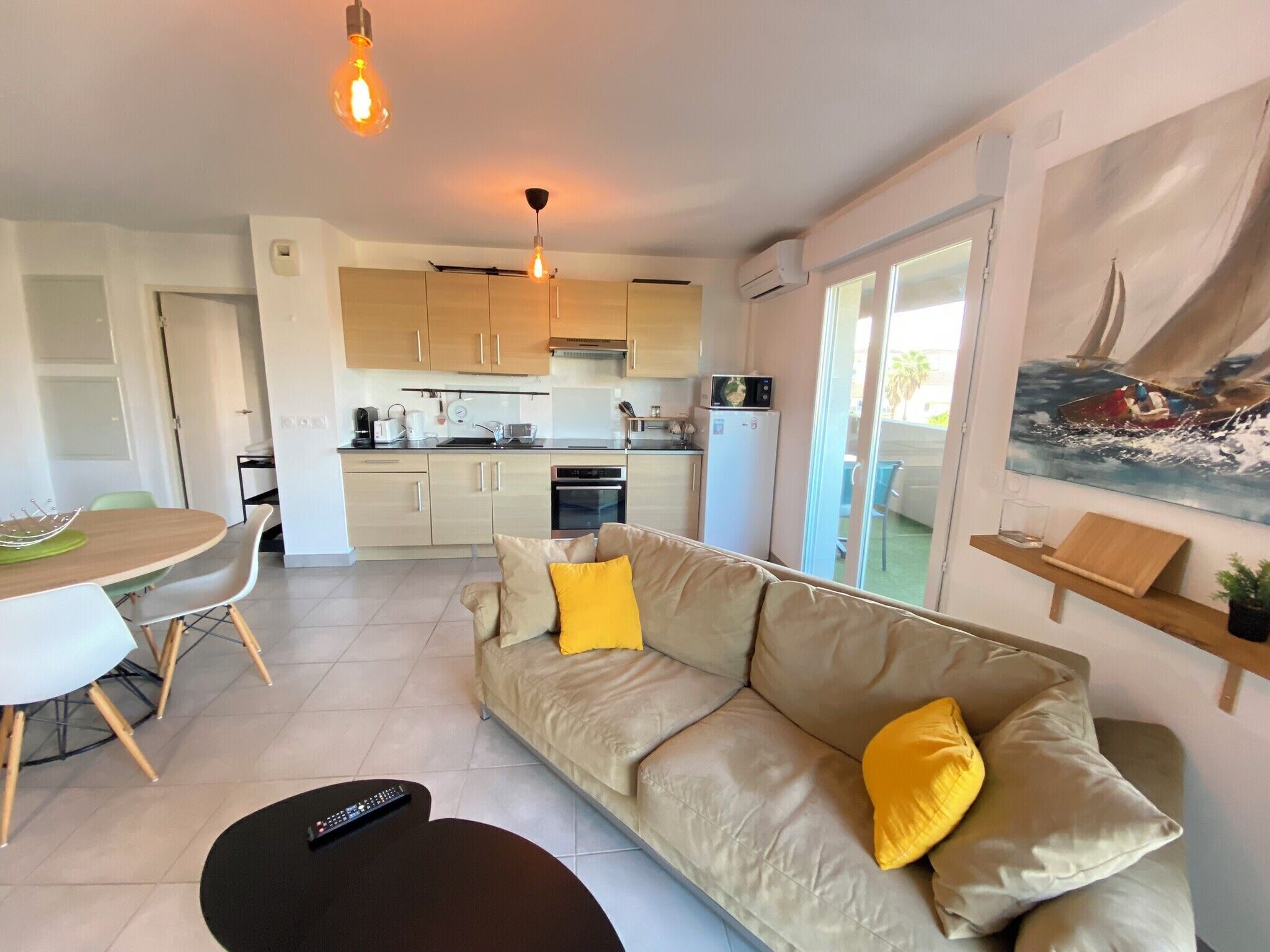 A modern living room with a beige sofa, a dining table, and a kitchen in the background.