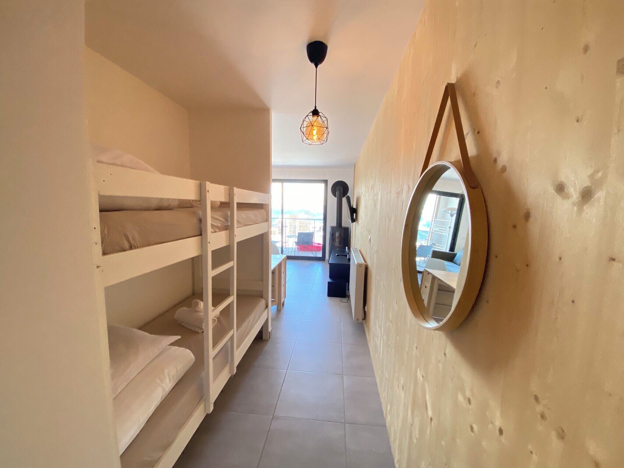 A narrow hallway with bunk beds on the left and a wooden wall with a round mirror on the right.