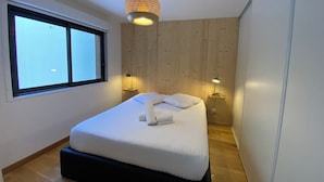 A modern bedroom with a large bed, two bedside lamps, a wooden wall panel, and a window.