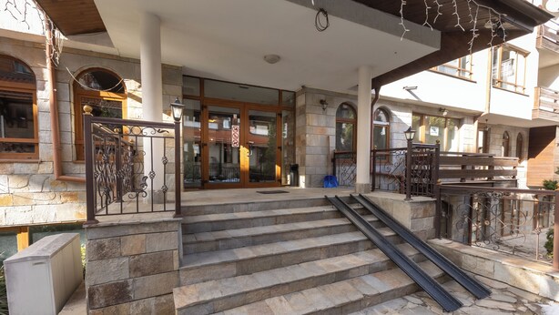 A stone staircase leading to a building entrance with metal railings and a clear view of the interior through the glass doors.
