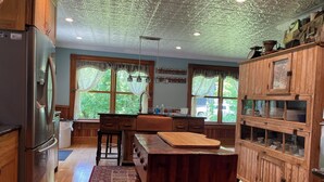 A kitchen with wooden cabinets, a stainless steel refrigerator, a wooden dining table, and a window with a view of greenery. - Thousand Island Park home, 5 bedroom,  3 and 1/2 bath, with dock space!! (Fineview)