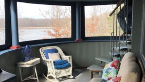 A cozy room with a wicker chair, a cushioned sofa, and a view of a lake through large windows. - Thousand Island Park home, 5 bedroom,  3 and 1/2 bath, with dock space!! (Fineview)
