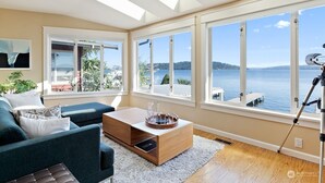 Una sala de estar moderna con sofá, mesa de centro y grandes ventanales con vista a un cuerpo de agua.
