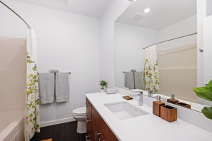 A modern bathroom with a white sink, a mirror, and a shower curtain with a leaf pattern.