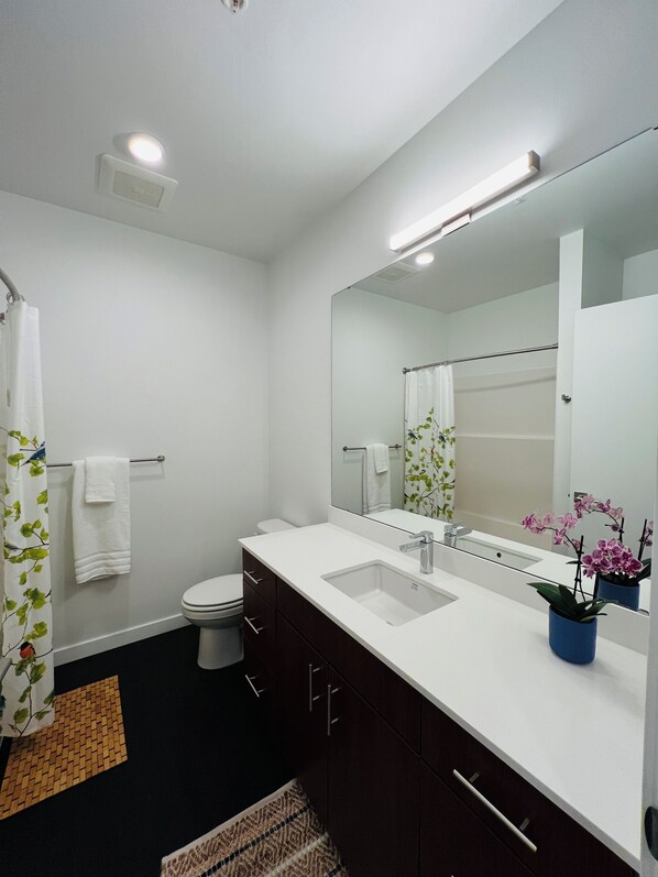 A modern bathroom with a white sink, dark wooden cabinets, a large mirror, and a shower curtain with a leaf pattern.