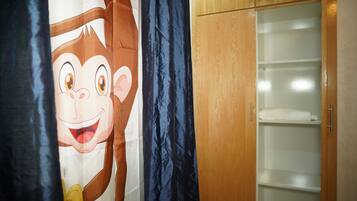 Une pièce avec une armoire en bois, un rideau orné d’un personnage de dessin animé et une étagère blanche.