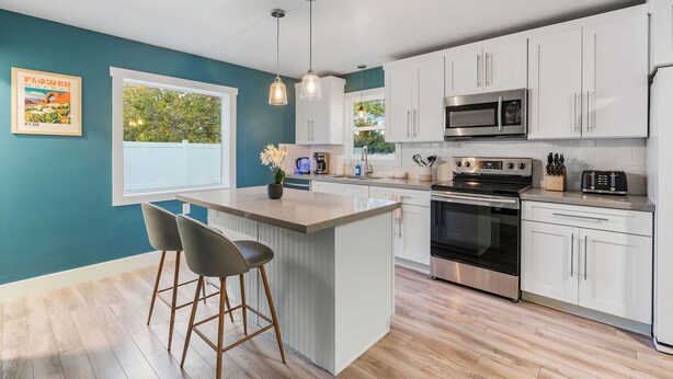 Una cocina moderna con armarios blancos, electrodomésticos de acero inoxidable y una isla central con taburetes de bar.