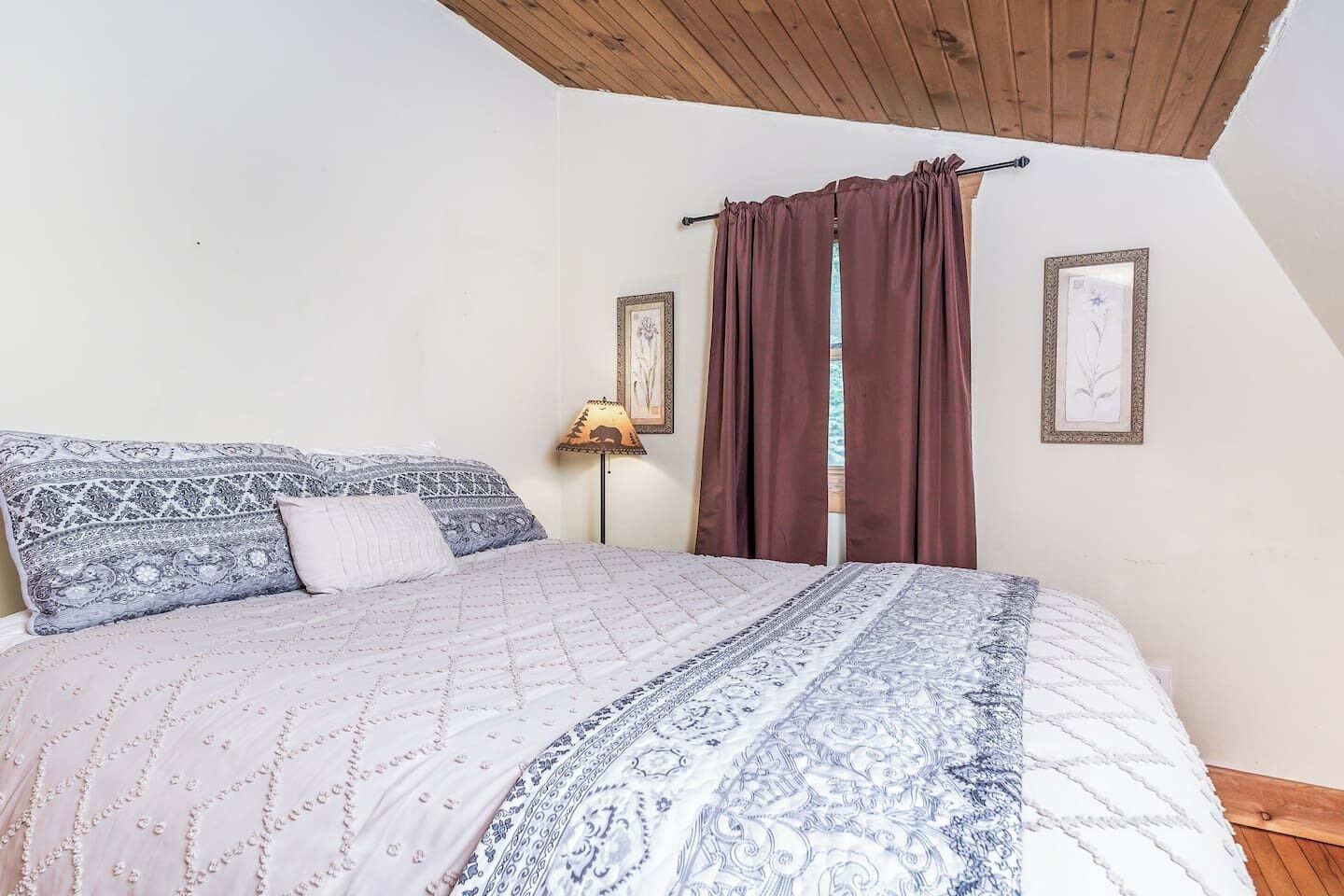 A bedroom with a bed, a lamp, and two framed pictures on the wall.