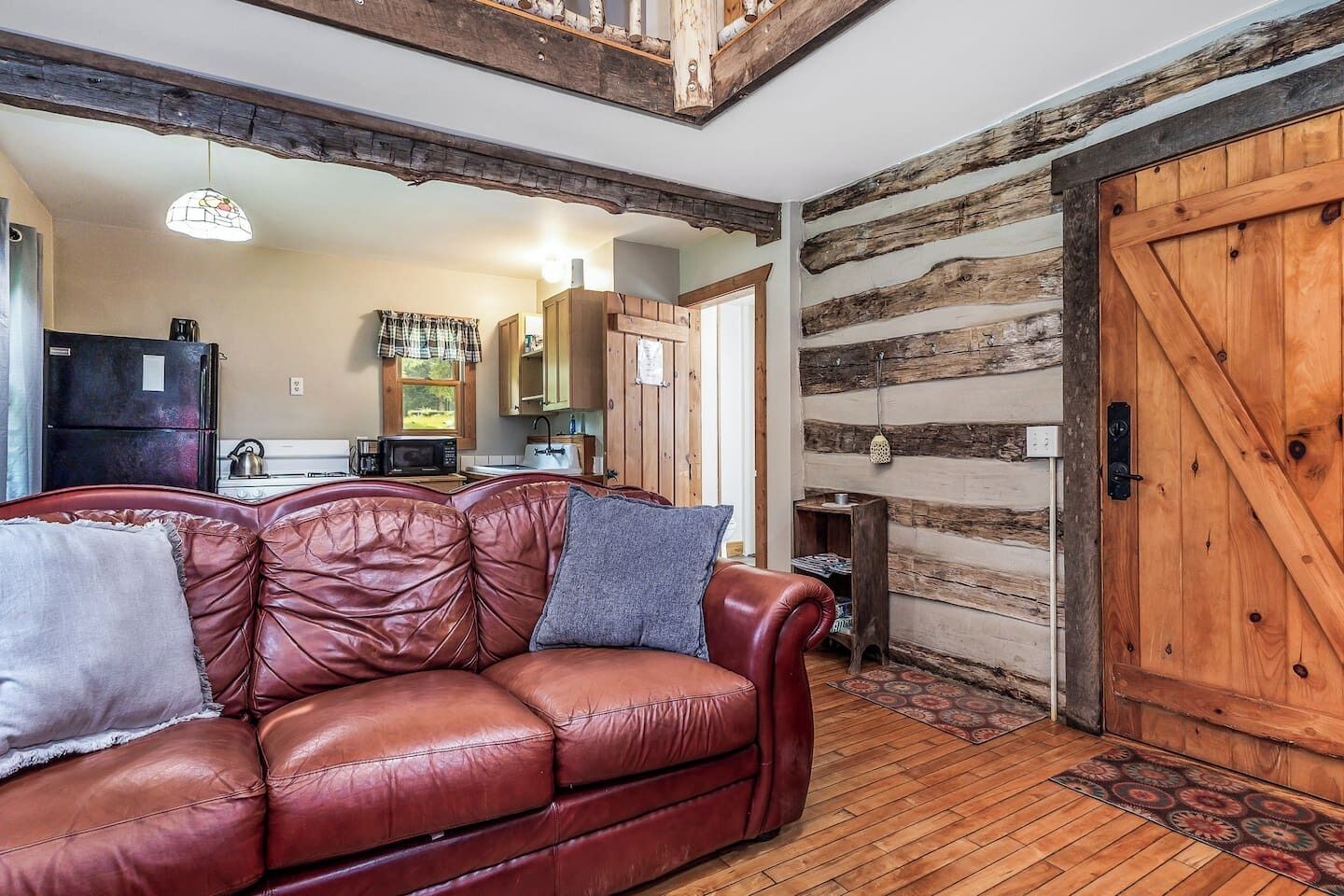 A cozy living room with a leather sofa, wooden walls, and a rustic kitchen in the background.