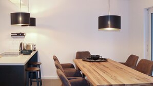 Une cuisine moderne avec une table à manger en bois, des tabourets de bar et des luminaires suspendus.