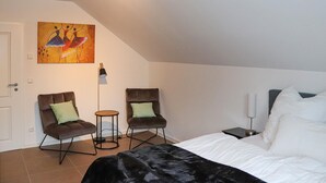 Une chambre à coucher avec un lit, deux fauteuils, une petite table, un tableau et une lampe.